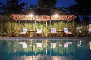 Un área junto a la piscina con una zona de estar cubierta y sillas de descanso.