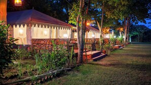 A row of rustic cabins with stone walls and metal roofs, surrounded by trees and a well-maintained lawn. - Maa Ashapura Resort (Sawai Madhopur)
