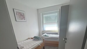 A small, compact room with a single bed, a window with blinds, a door, and a small table. - Red Dot Eva (Werne)