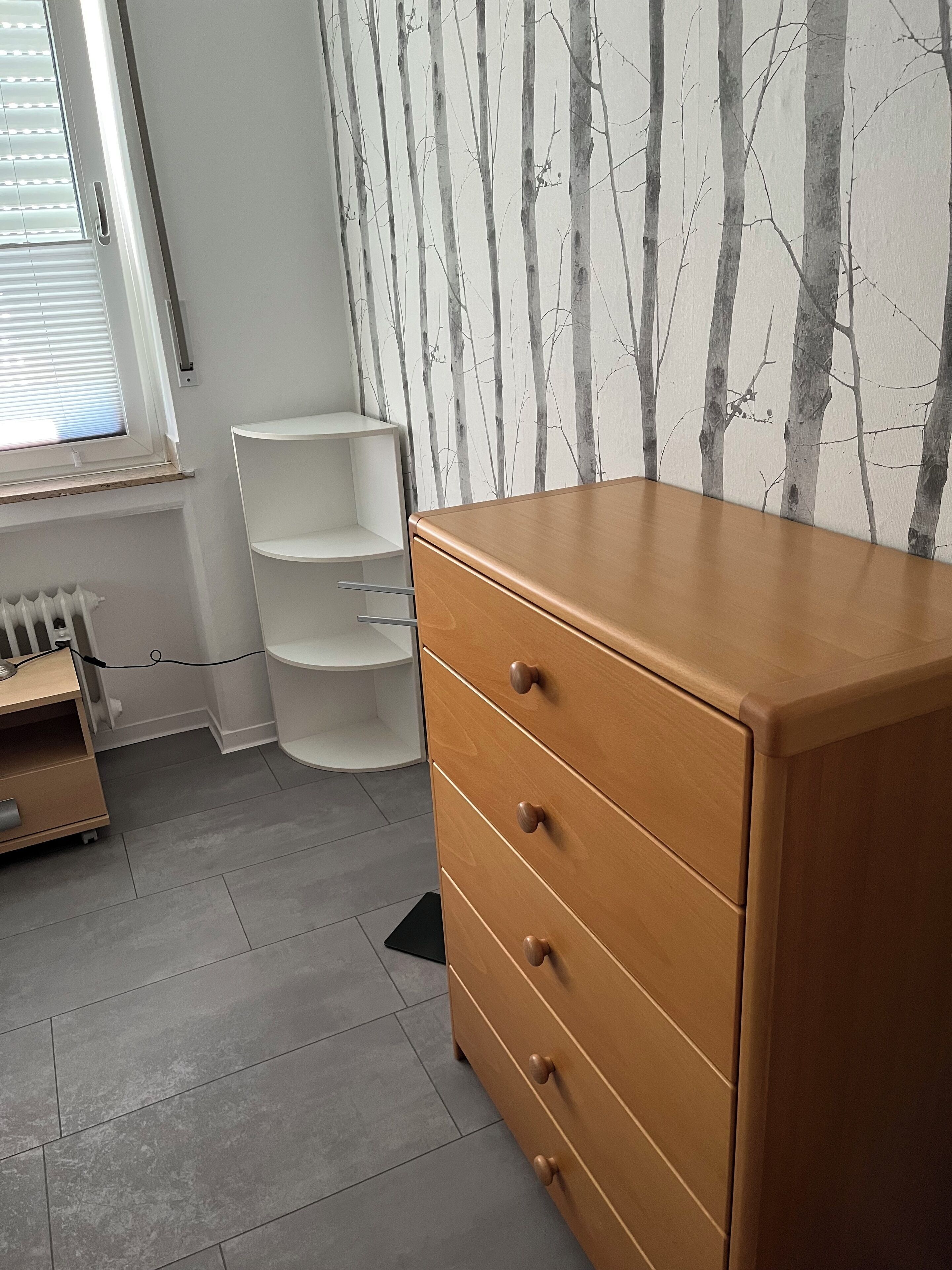 A room with a wooden dresser, white shelving unit, and a radiator.