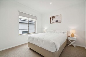 Une chambre à coucher avec un grand lit, une fenêtre, une table de chevet avec une lampe et un tableau accroché au mur.