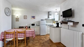 Cocina compacta con una mesa de comedor, sillas, un reloj, microondas, refrigerador, estufa y un televisor.