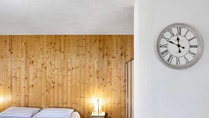 Un dormitorio con cabecera de madera, cama con ropa de cama a rayas, lámpara de noche y un reloj de pared.