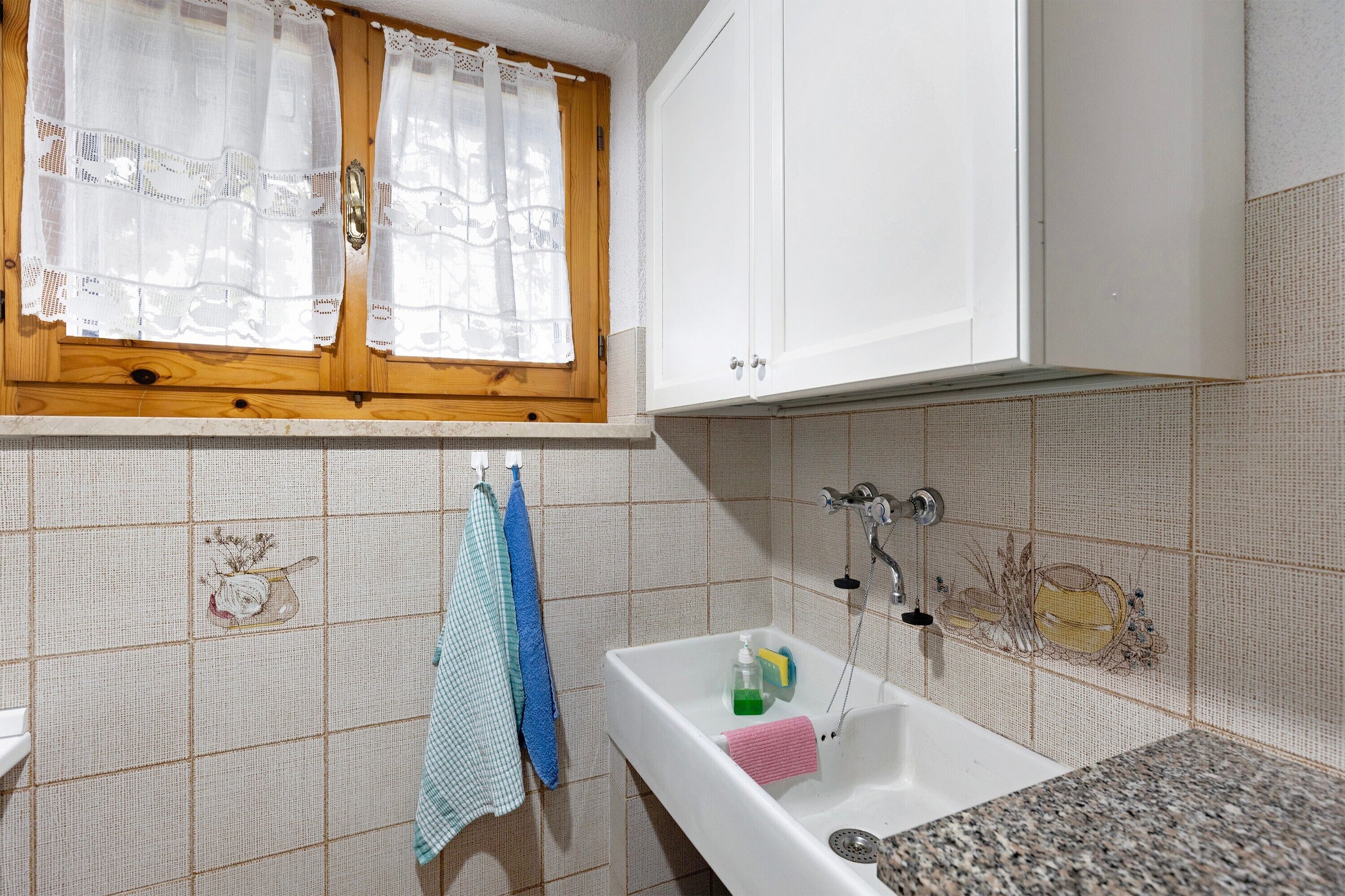 Un bany amb un lavabo, finestra amb cortines i un escurapulides.