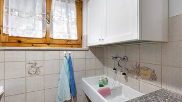 Un bany amb un lavabo, finestra amb cortines i un escurapulides.