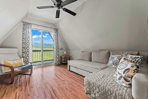 A room with a ceiling fan, a sofa, a chair, and a view of the outdoors.