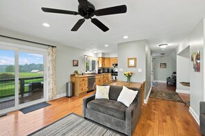 A spacious living room with a grey sofa, a ceiling fan, and a view of a kitchen and dining area. - Sojourners Rest: Old Rag Views, Hot Tub, Fire Pit (Etlan)