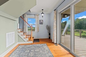 A spacious room with a wooden staircase, a large sliding glass door leading to an outdoor deck, and a hanging light fixture. - Sojourners Rest: Old Rag Views, Hot Tub, Fire Pit (Etlan)