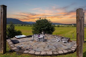 A circular outdoor patio with stone flooring, surrounded by wooden posts, featuring a hot tub, a table with chairs, and a large tree. - Sojourners Rest: Old Rag Views, Hot Tub, Fire Pit (Etlan)