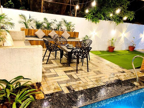 An outdoor patio with a pool, surrounded by potted plants and string lights. - Tokyo Villa By Staymatic Villa's (Mawal)