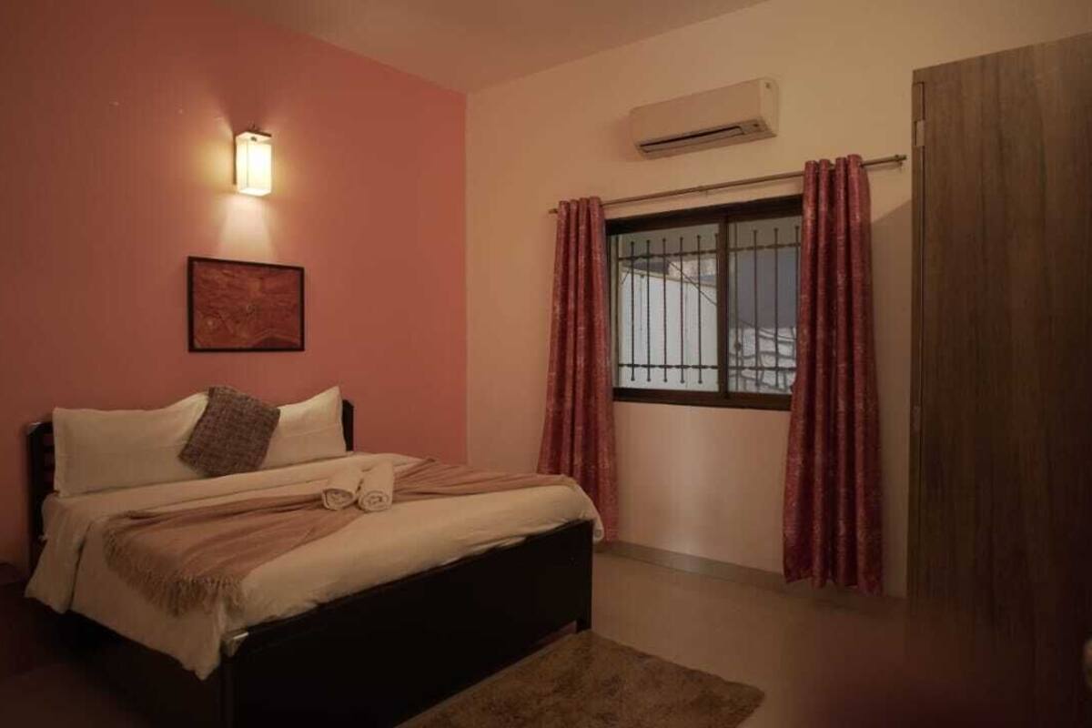 Ein Schlafzimmer mit einem Bett, einer Wandklimaanlage, einem Fenster mit Vorhängen und einer Tür.