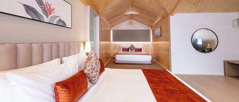 Un dormitorio moderno con una cama grande, una cama más pequeña al fondo, techo de madera y un espejo redondo en la pared.
