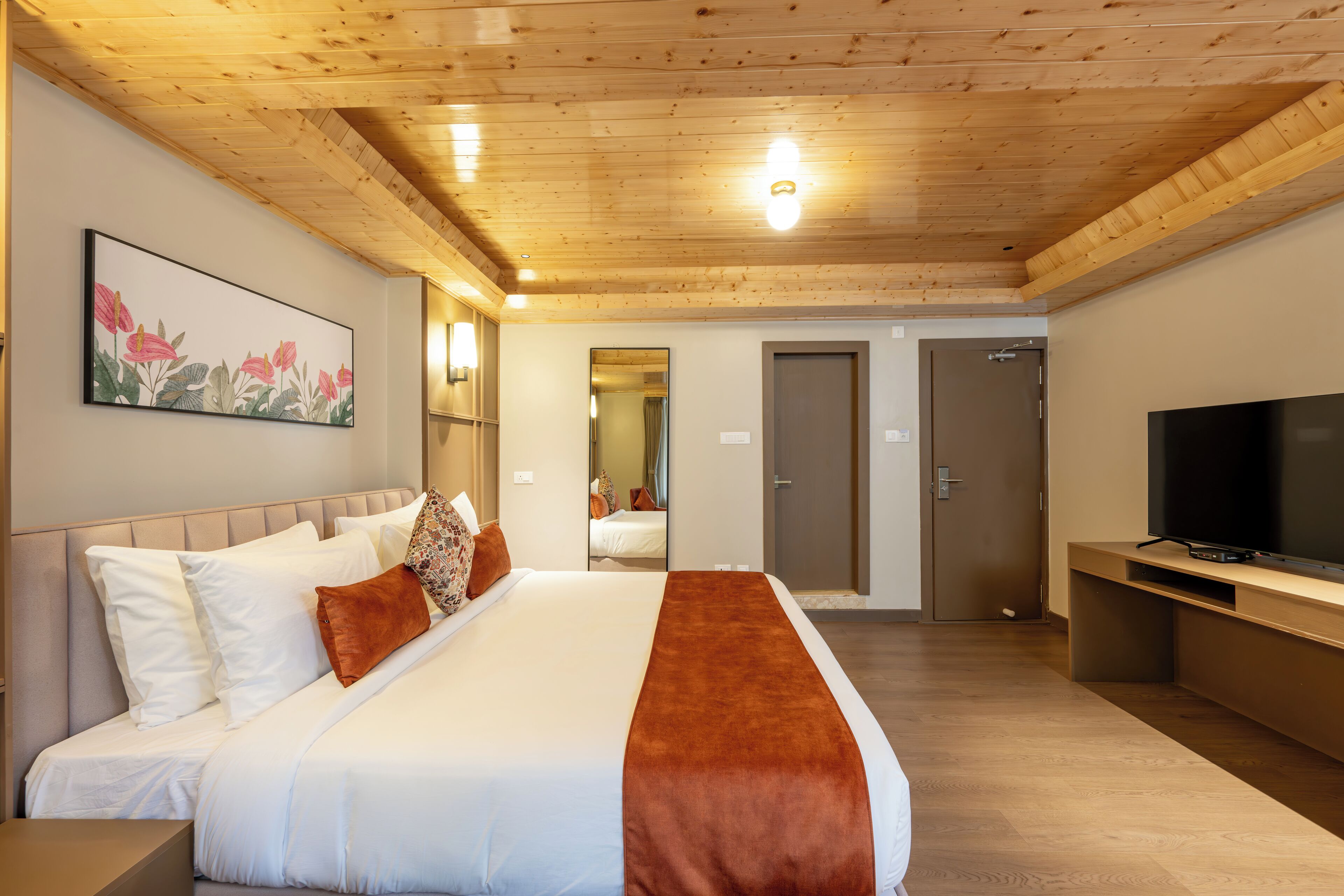 A hotel room with a large bed, wooden ceiling, a TV, and a painting on the wall.
