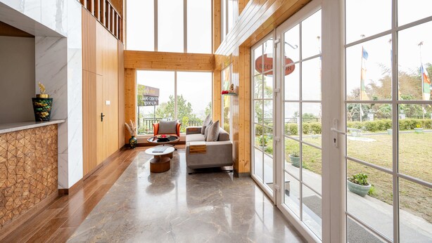 A spacious interior with a high ceiling, wooden beams, a seating area with a sofa and chairs, and large windows offering a view of the outdoors. - Udaan Khang-Chen View Resort & Spa (Gyalshing)