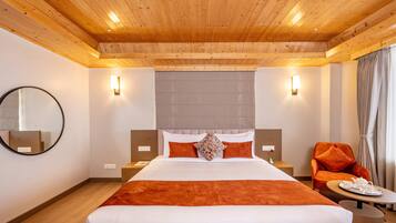 A hotel room with a wooden ceiling, a large bed with orange bedding, a round mirror, two bedside tables, a chair, and a small table with a tray.