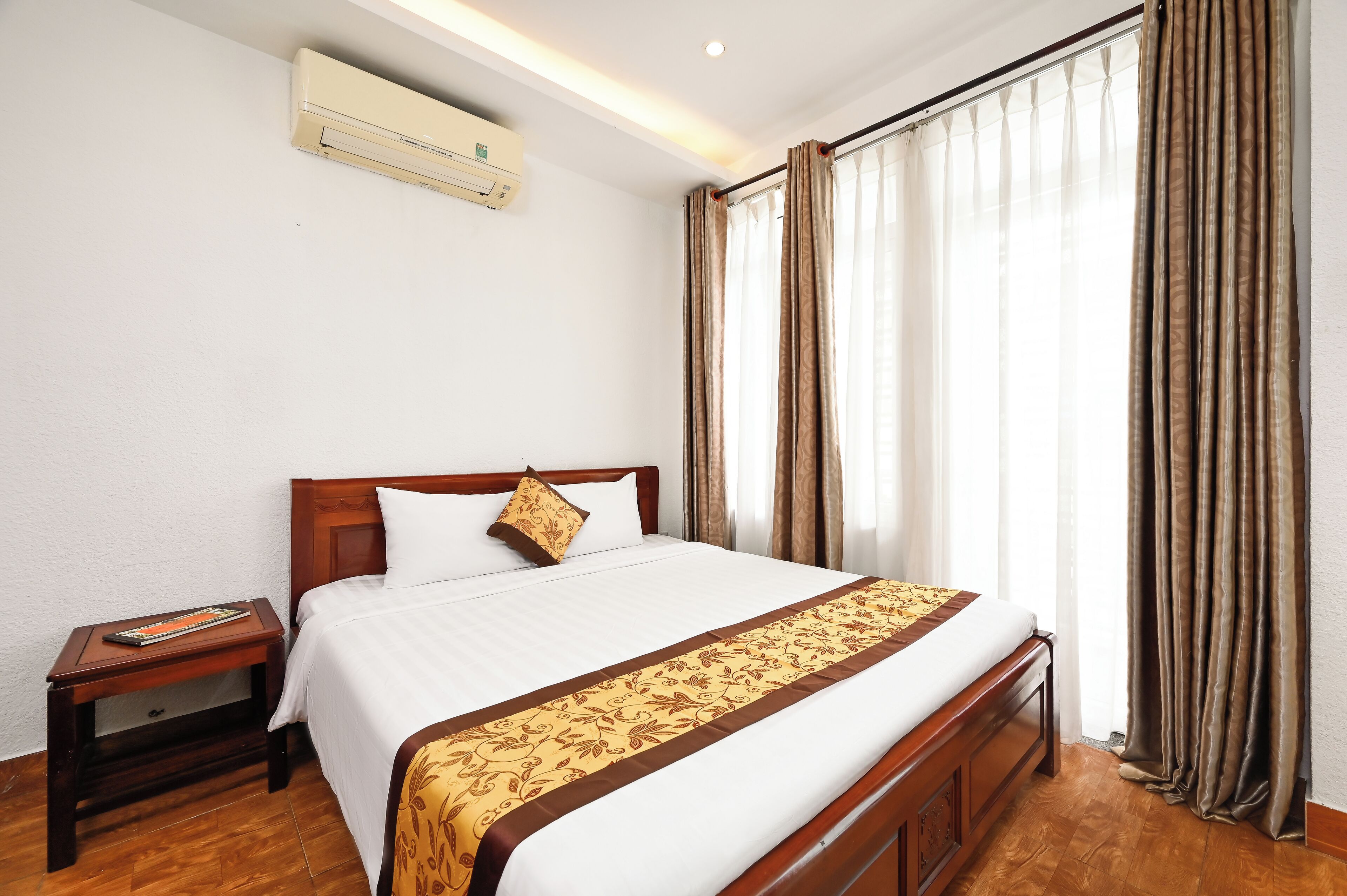 A neatly made bed with a white and brown bedspread, a wooden headboard, and a nightstand with a magazine.