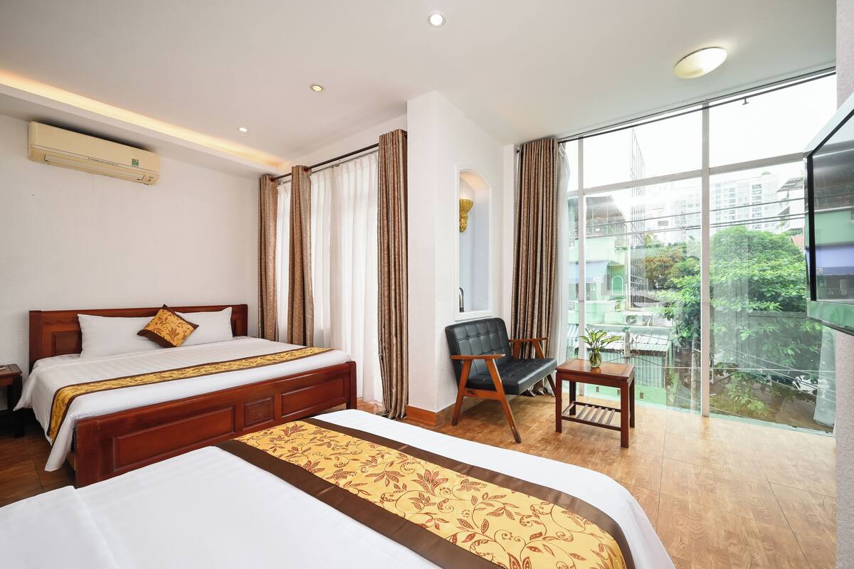 Une chambre d’hôtel avec deux lits, un bureau, une chaise et une grande fenêtre donnant sur la ville.