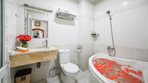 A bathroom with a toilet, sink, and bathtub filled with rose petals. - Queen Hotel Saigon Airport (Ho Chi Minh City)