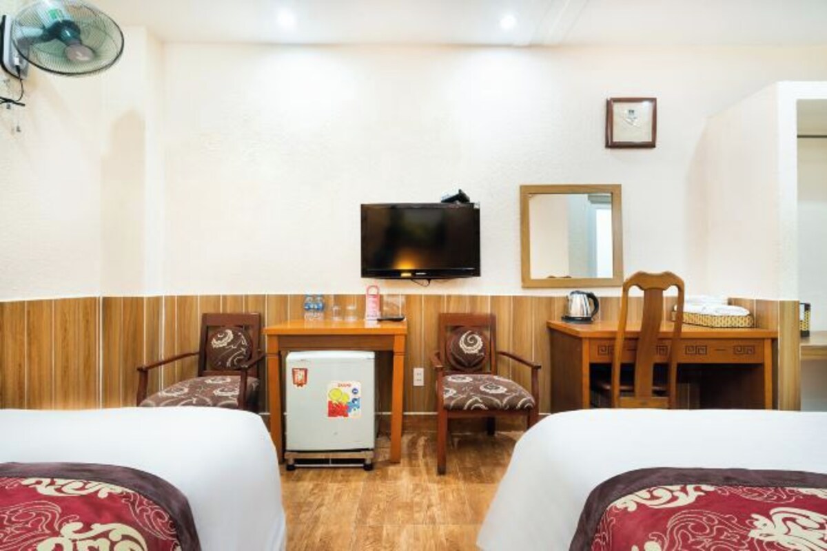 A hotel room with two beds, a desk with a chair, a small refrigerator, a television mounted on the wall, and a wooden cabinet.