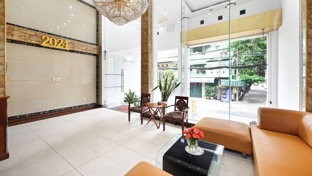 A modern hotel lobby with a large '2024' sign, a chandelier, seating area, and a view of the street outside. - Queen Hotel Saigon Airport (Ho Chi Minh City)