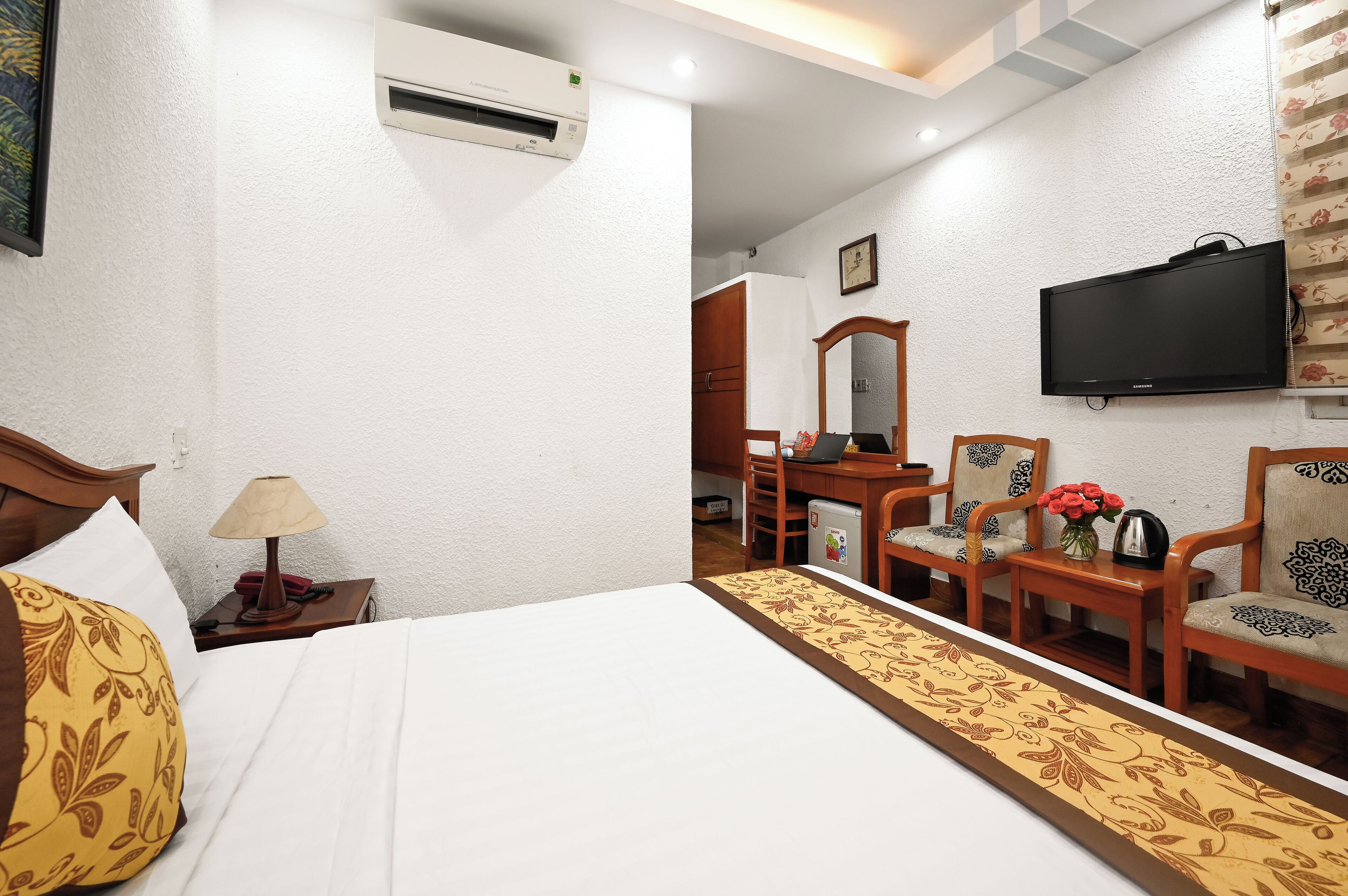 A hotel room with a bed, a desk, a chair, a television, and an air conditioning unit.
