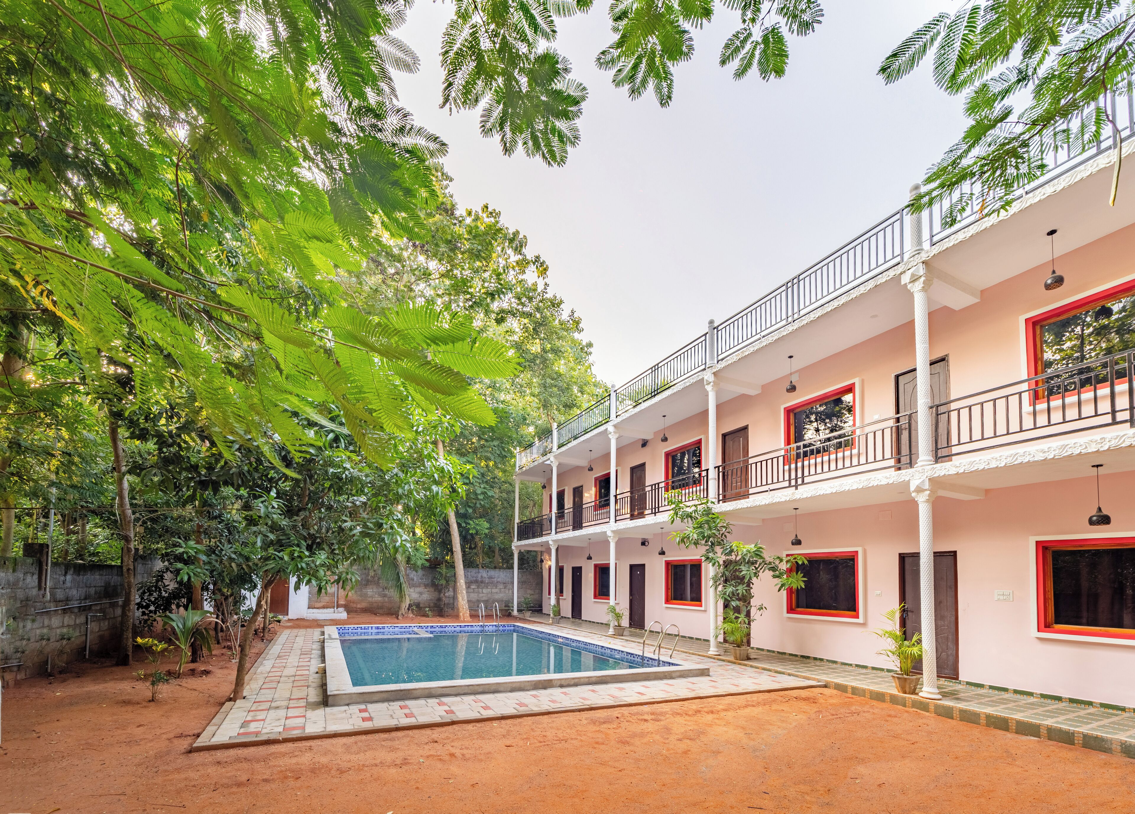 A two-story building with a swimming pool, surrounded by lush greenery and trees.