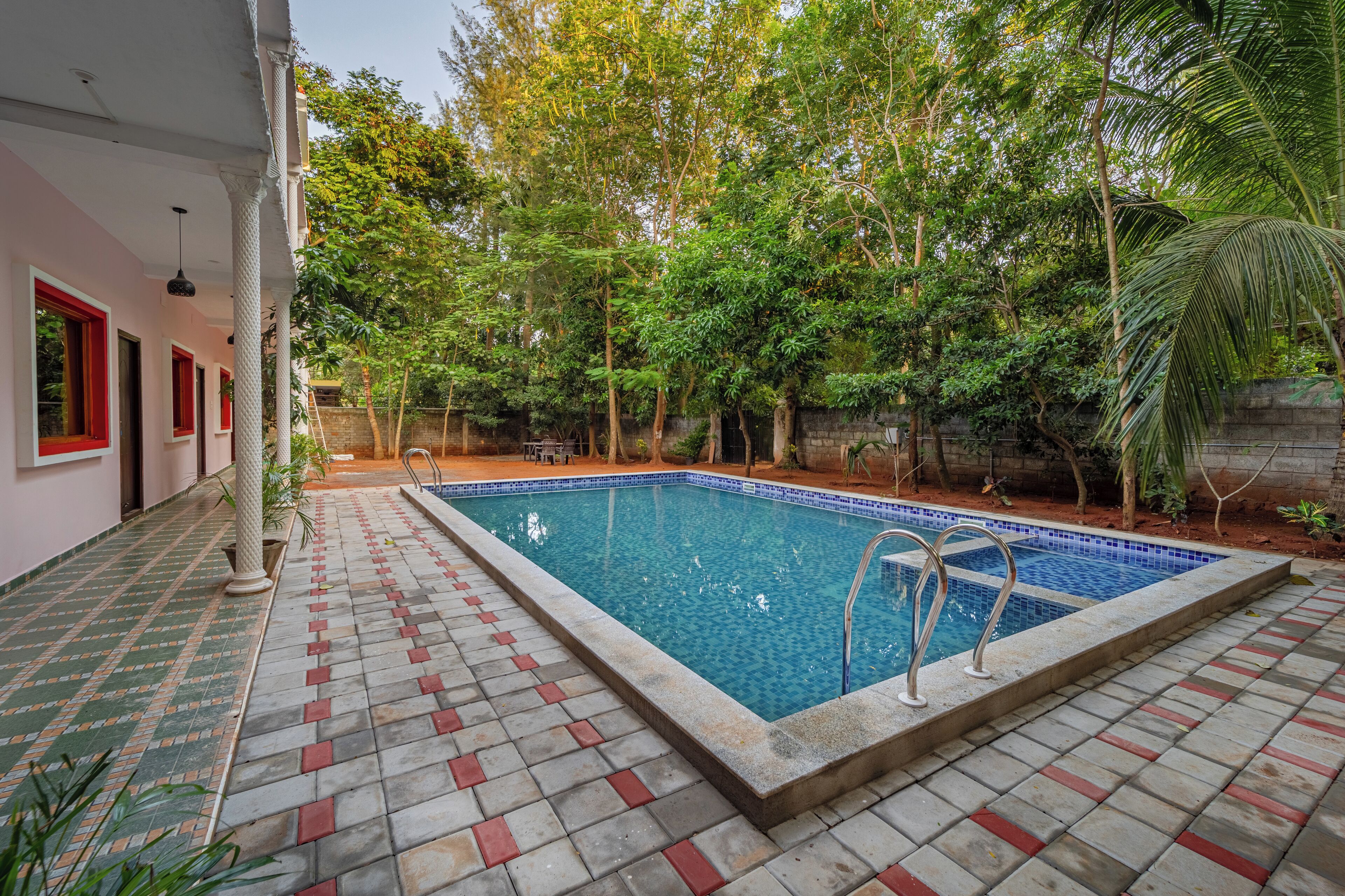 A rectangular swimming pool with a tiled edge, surrounded by a tiled patio with red accents.