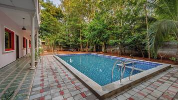 A rectangular swimming pool with a tiled edge, surrounded by a tiled patio with red accents.