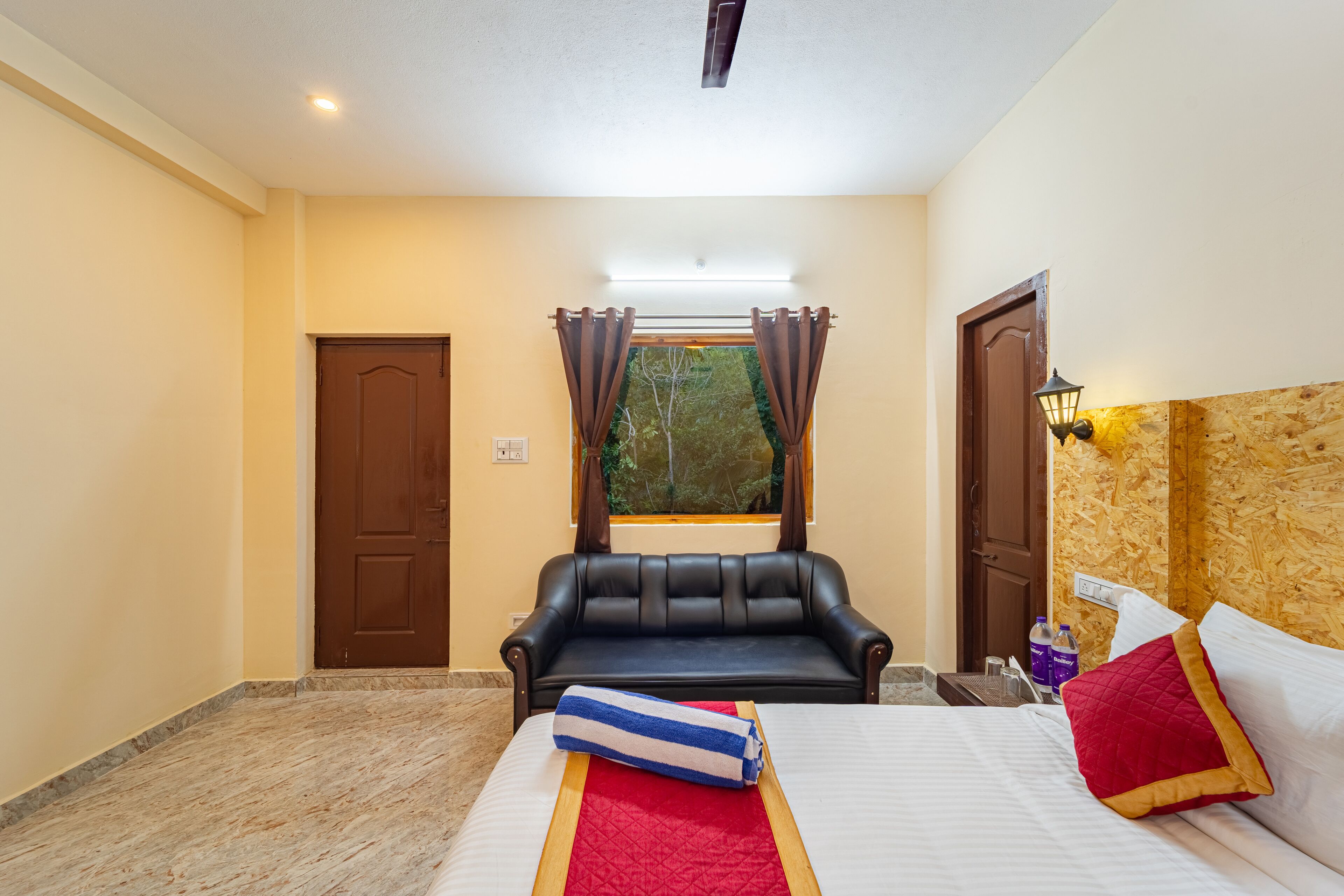 A hotel room with a bed, a sofa, a window with curtains, and a wooden wall.