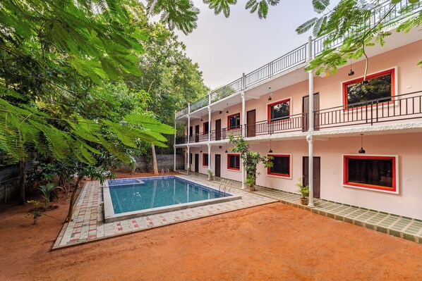 A two-story building with a swimming pool, surrounded by lush greenery.