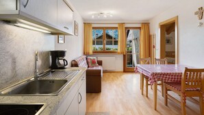 A kitchen with a sink, stove, and coffee maker, a dining area with a table and chairs, and a window with curtains. - Apartment 'Inneroswalderhof  3' with Mountain View, Shared Garden and Wi-Fi (Anterselva di Sotto)