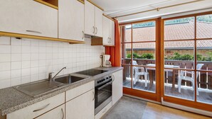 Une cuisine équipée d’un évier, d’une cuisinière et d’un four, une fenêtre donnant sur un toit recouvert de tuiles et des meubles d’extérieur.