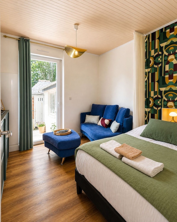 Un dormitorio con cama, sofá, suelo de madera, luz en el techo y vista por una puerta.