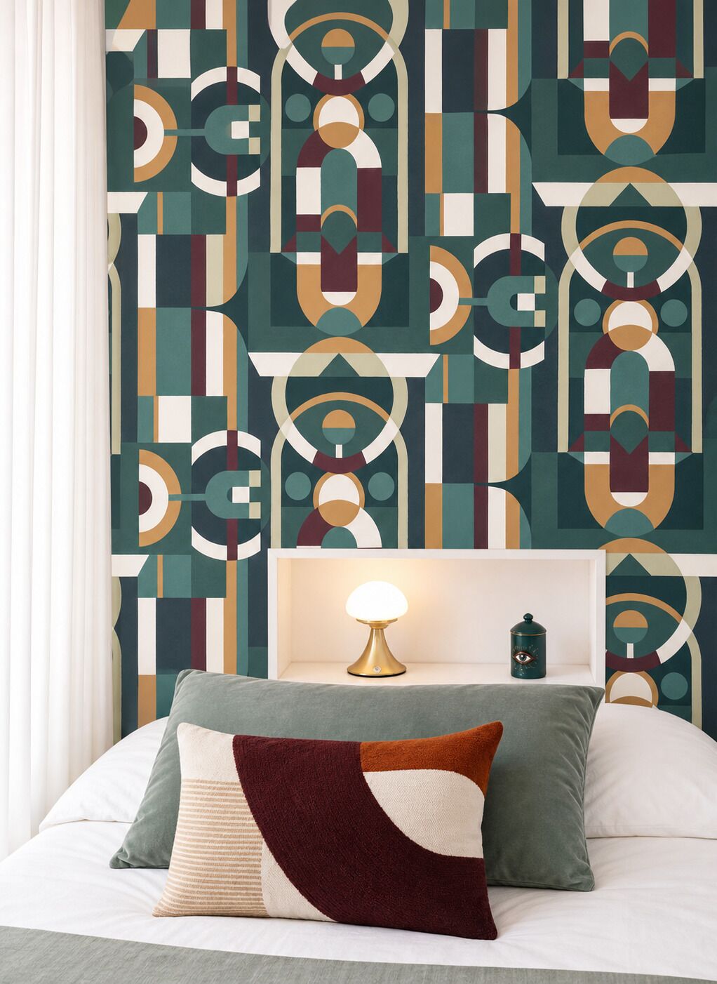 Een slaapkamer met een wand met een geometrisch patroon, een nachtkastje met een lamp en een bed met kussens.