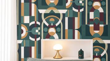 A bedroom with a geometric patterned wall, a bedside table with a lamp, and a bed with pillows.