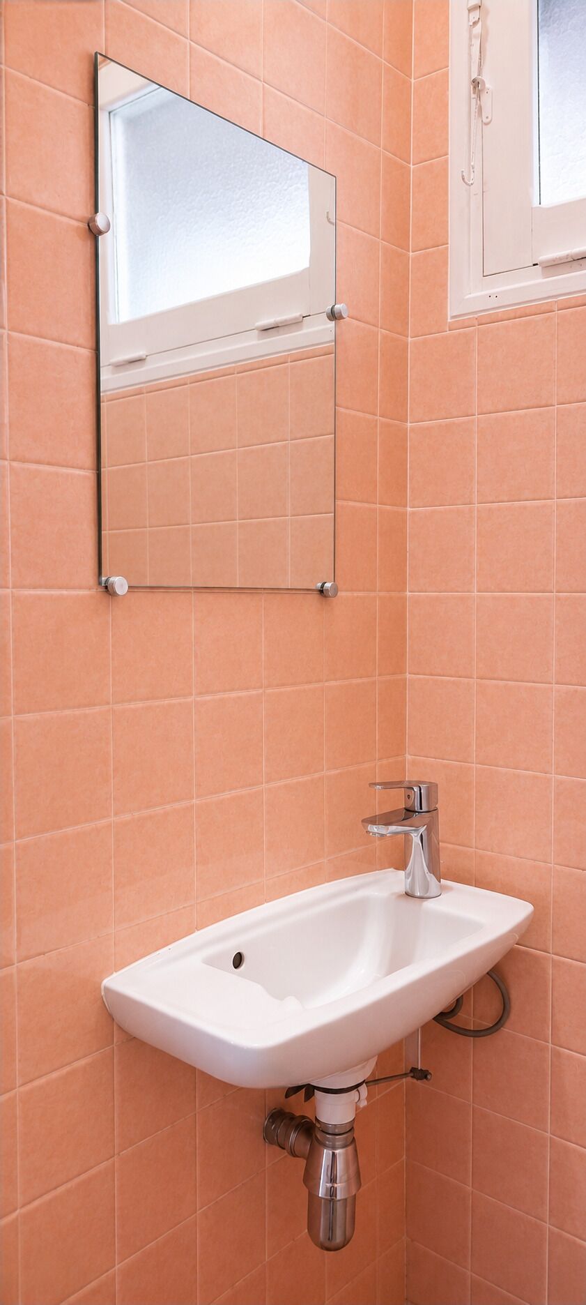 Un baño con lavamanos blanco, un espejo y paredes con azulejos naranjas.