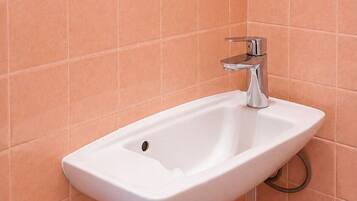Un baño con lavamanos blanco, un espejo y paredes con azulejos naranjas.