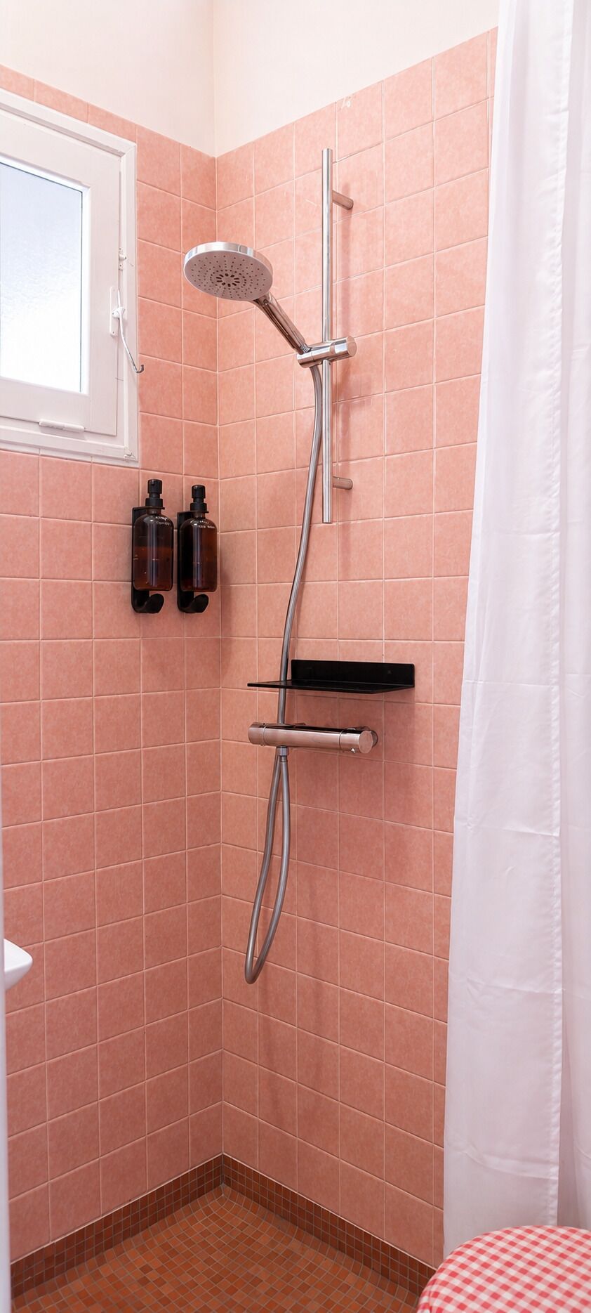 Une douche équipée d’un pommeau de douche à main, d’un panneau de commande mural et d’une étagère pour les articles de toilette.
