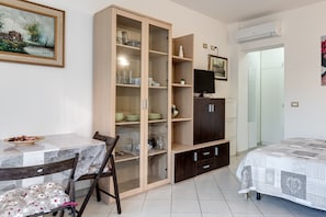 Une pièce comprenant une table à manger, des chaises, un meuble avec des portes en verre, un lit et un appareil de climatisation.