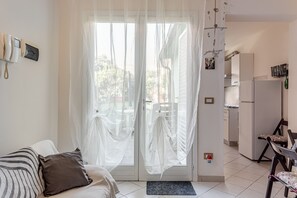 Une pièce comprenant un lit, une chaise, un coin cuisine et une porte avec des rideaux légers.