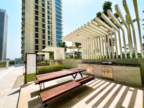 An outdoor patio with wooden benches, a built-in barbecue grill, and a pergola structure.