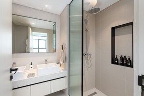 A modern bathroom with a glass-enclosed shower, a large mirror, and a shelf with toiletries.