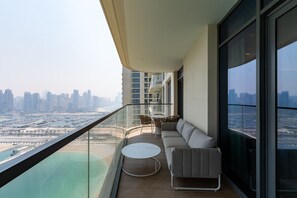 Un balcón con sofá, una mesa redonda y una silla, con vistas a un paisaje urbano y una masa de agua.