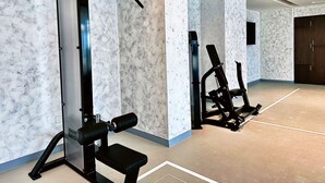 Een fitnessruimte met krachttrainingsapparatuur en een bank, muren met een marmerpatroon, en een grote donkerhouten deur.