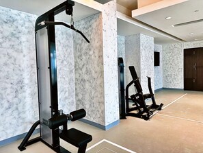 Een fitnessruimte met krachttrainingsapparatuur en een bank, muren met een marmerpatroon, en een grote donkerhouten deur.