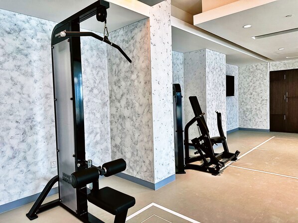 A gym with weight machines and a bench, marble-patterned walls, and a large dark wooden door.