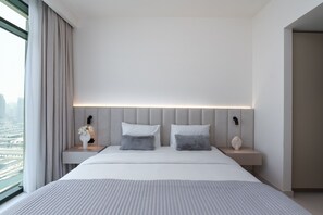 Een moderne hotelkamer met een groot bed, twee nachtkastjes, een bloevas en uitzicht op een stadsgezicht door een groot raam.