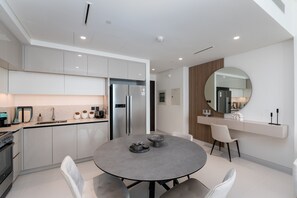 Una cocina moderna con armarios blancos, un refrigerador de acero inoxidable y una mesa de comedor redonda con sillas.