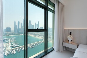 Una habitación de hotel moderna con un ventanal grande que ofrece vistas a un puerto deportivo y al horizonte de la ciudad.