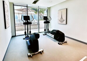 A gym with cardio machines, dumbbells, and a large window with a view of buildings and greenery.